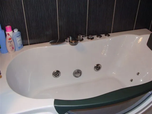 Weiße Whirlpool-Badewanne in einem modernen Badezimmer einer Wohnung in Budva, Montenegro, mit dunkler Wandverkleidung.