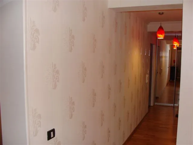 Heller Flur in einer Wohnung in Budva, Montenegro: gemusterte Tapete, Holzboden und rote Deckenleuchten.