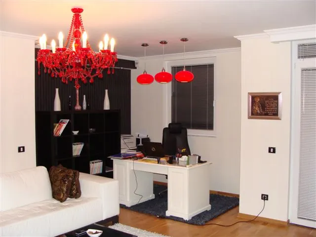 Modernes Wohnzimmer mit Arbeitsplatz in einer Wohnung in Budva, Montenegro: weiße Möbel, roter Kronleuchter und Parkettboden.