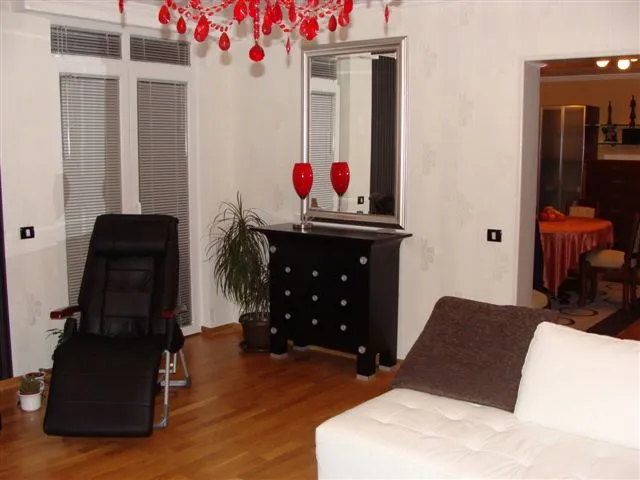Wohnzimmer in einer Wohnung in Budva, Montenegro: helles Interieur, schwarze Möbel, Spiegel und roter Kronleuchter, Parkettboden.