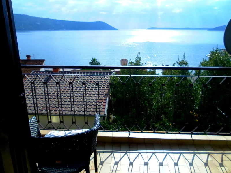 Balkon mit Korbstuhl, Geländer, Fliesenboden und Meerblick.