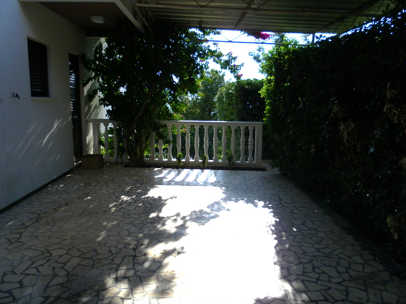 Ugodna natkrivena terasa sa kamenim podom i balustradom u kući u Herceg Novom, Crna Gora, okružena zelenilom.