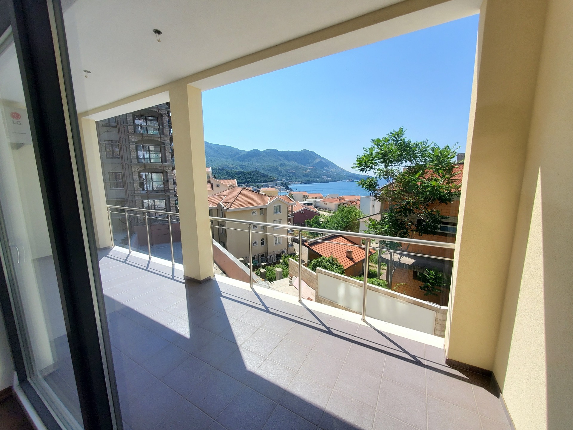 MonteDreams konut kompleksinde, Bečići, Karadağ’da deniz ve dağ manzaralı geniş balkon: fayans zemin ve cam korkuluklar.