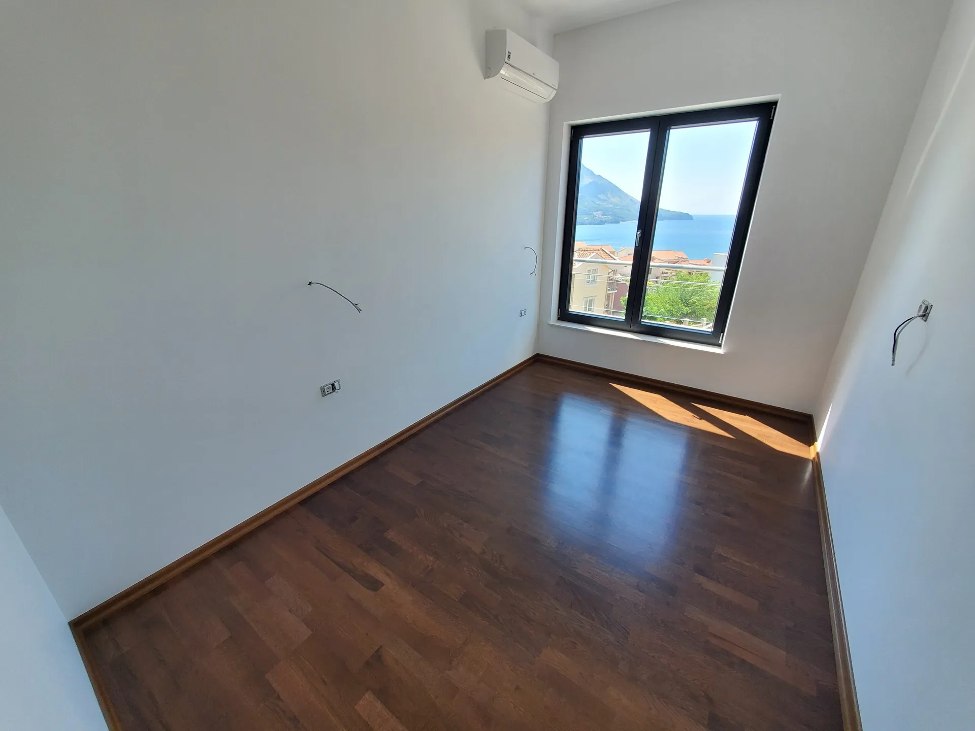 Leeres, helles Schlafzimmer mit dunklem Parkettboden und einem Fenster mit Meerblick