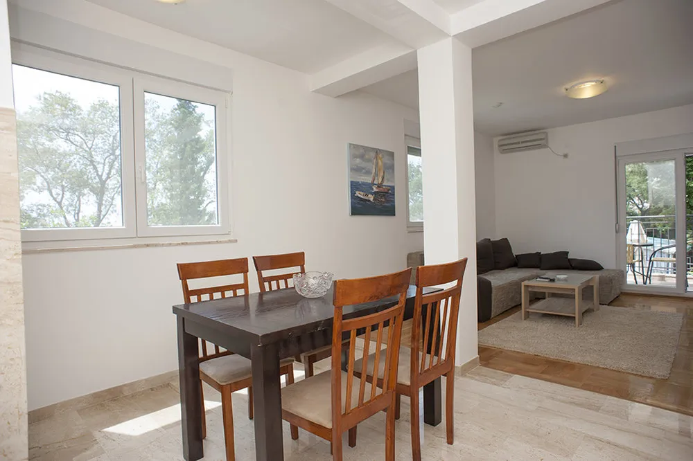 Wohnzimmer mit Essbereich in einer Villa in Perazica Do, Montenegro: dunkler Holztisch, helle Möbel und Blick auf den Garten.