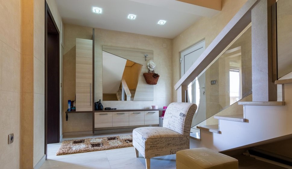 Moderne Diele in einer Villa in Tivat, Montenegro: helle Möbel, Spiegel, Treppe mit Glasgeländer.