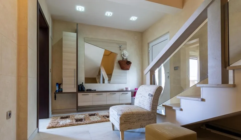 Moderne Diele in einer Villa in Tivat, Montenegro: helle Möbel, Spiegel, Treppe mit Glasgeländer.