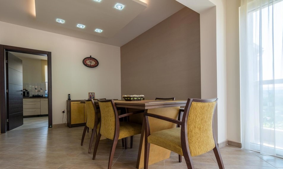 Modernes Wohnzimmer mit Essbereich in einer Villa in Tivat, Montenegro: Holztisch, gelbe Stühle und Spotbeleuchtung.