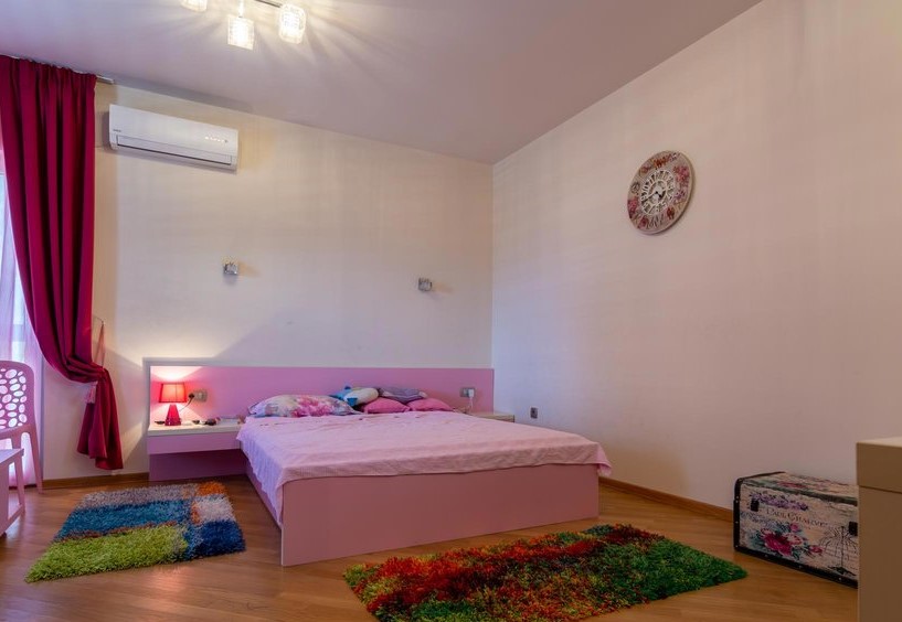 Schlafzimmer mit rosa Bett und bunten Teppichen in einer Villa in Tivat, Montenegro. Helle Ausstattung, Klimaanlage und Dekor.