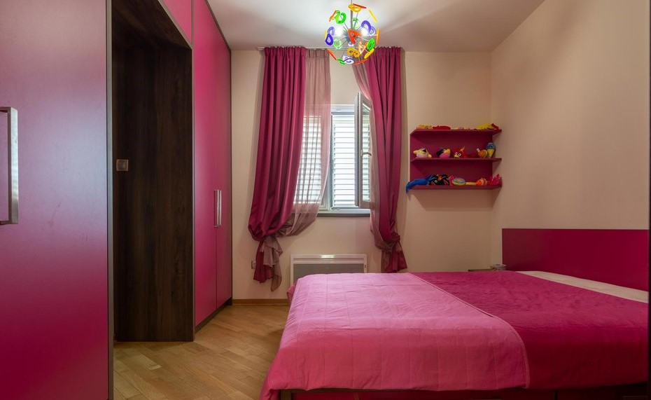 Helles Kinderzimmer mit rosa Möbeln und Bett in einer Villa in Tivat, Montenegro. Parkettboden, Fenster mit Vorhängen.