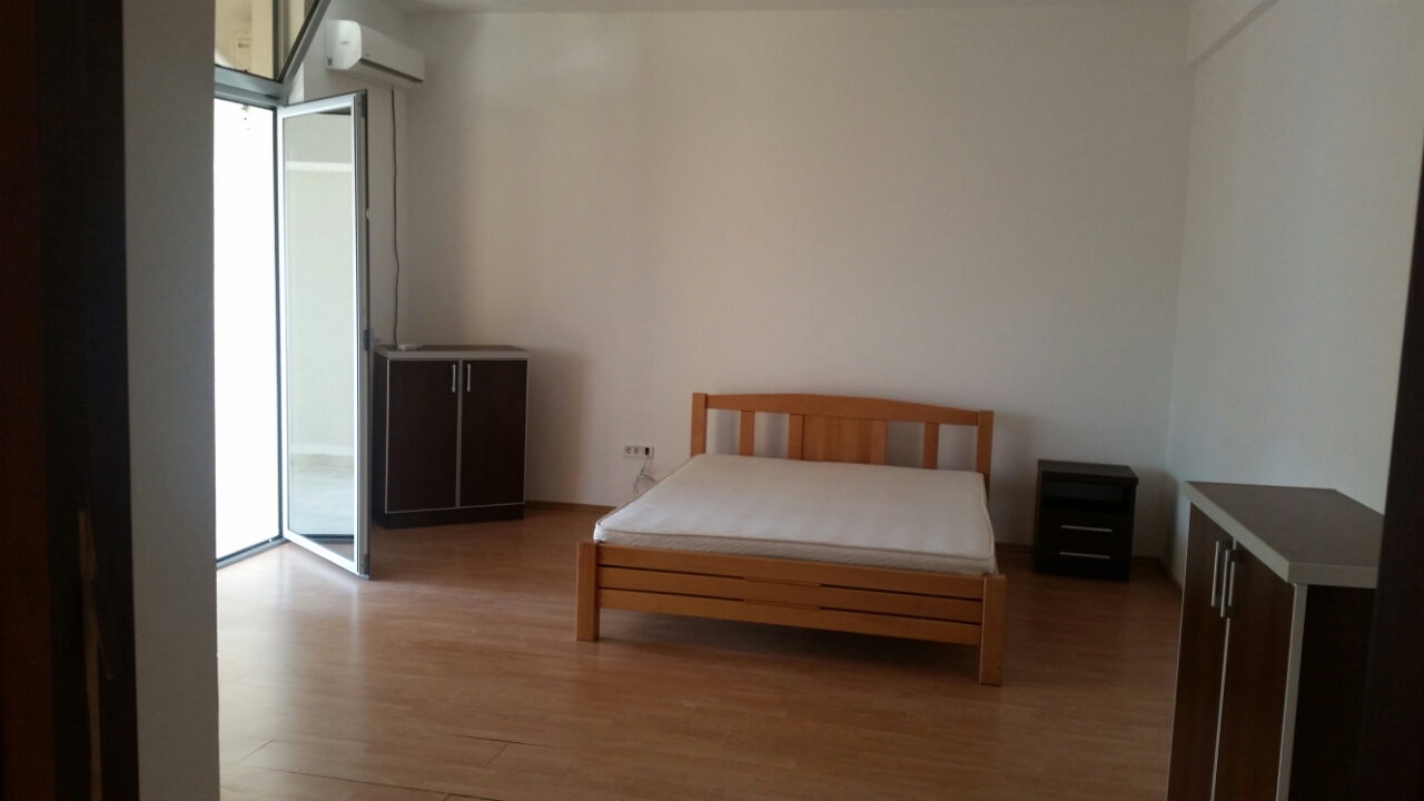 Svetla spavaća soba sa drvenim krevetom i izlazom na balkon u stanu, grad Budva, Crna Gora.