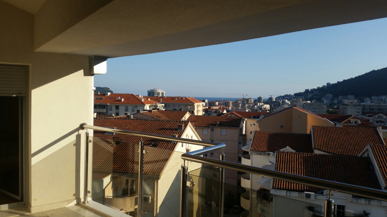 Pogled sa balkona stana u Budvi, Crna Gora: panorama grada sa krovovima od crepa i morskim horizontom.