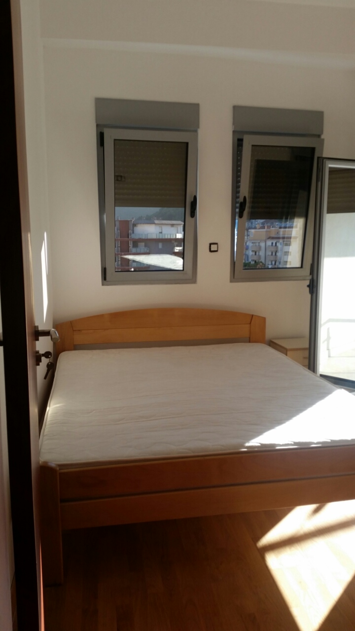 Svetla spavaća soba sa bračnim krevetom u stanu u Budvi, Crna Gora, sa izlazom na balkon i pogledom na grad.