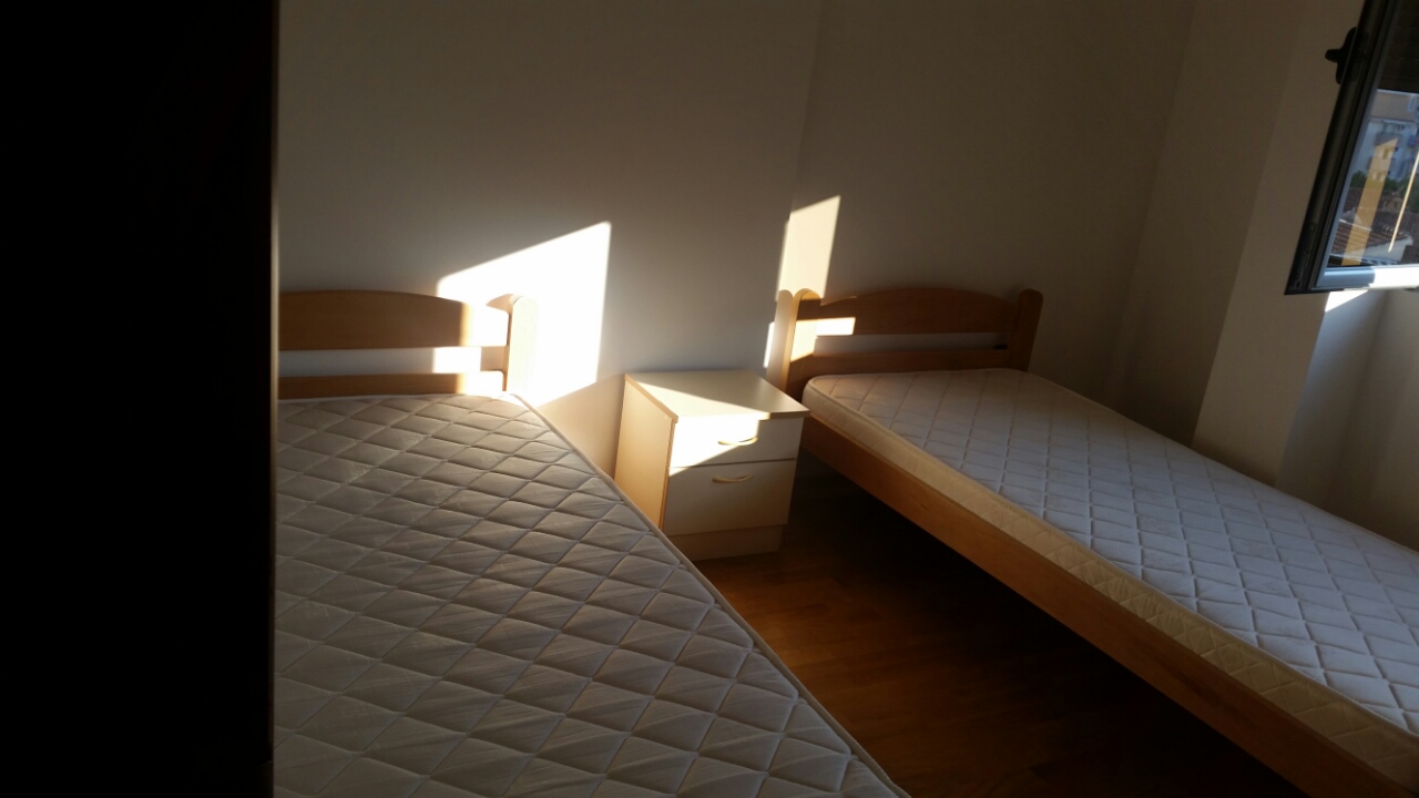 Svetla spavaća soba sa dva jednokrevetna kreveta i noćnim ormarićem u stanu, Budva, Crna Gora.
