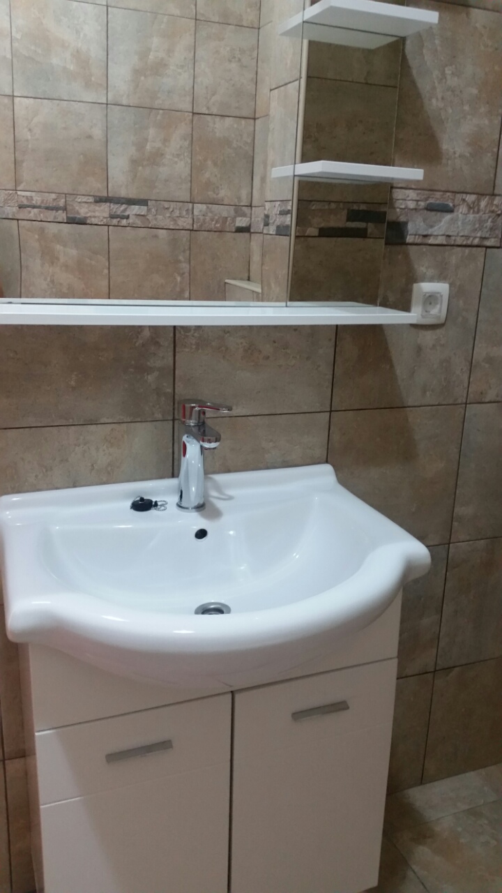 Kupatilo u stanu u Budvi, Crna Gora: bela komoda sa umivaonikom, hromirana slavina i pločice u imitaciji kamena.