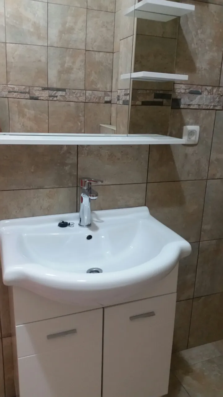 Badezimmer in einer Wohnung in Budva, Montenegro: weiße Waschtischkonsole mit Waschbecken, verchromter Wasserhahn und Steinoptik-Fliesen.