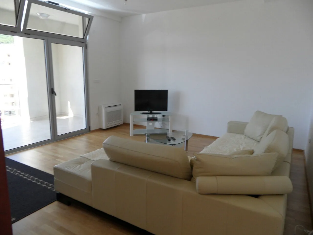 Helles Wohnzimmer mit beigem Sofa, TV und Zugang zur Terrasse in einer Wohnung in Budva, Montenegro.