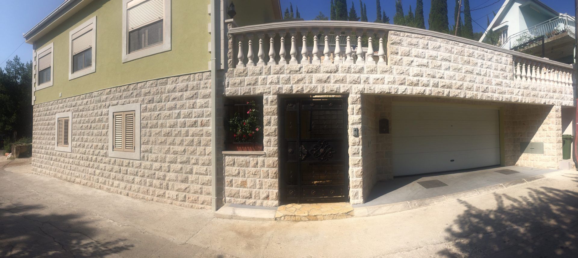 House facade in Zelenika, Montenegro: stone cladding, wrought-iron gates, garage, and a second-floor terrace with balustrade.