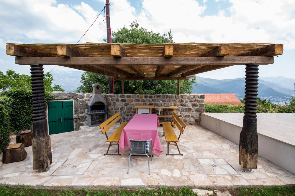 Überdachte Terrasse mit Grill und Essbereich in einer Villa in Luštica, Montenegro: Steinverkleidung und Bergblick.