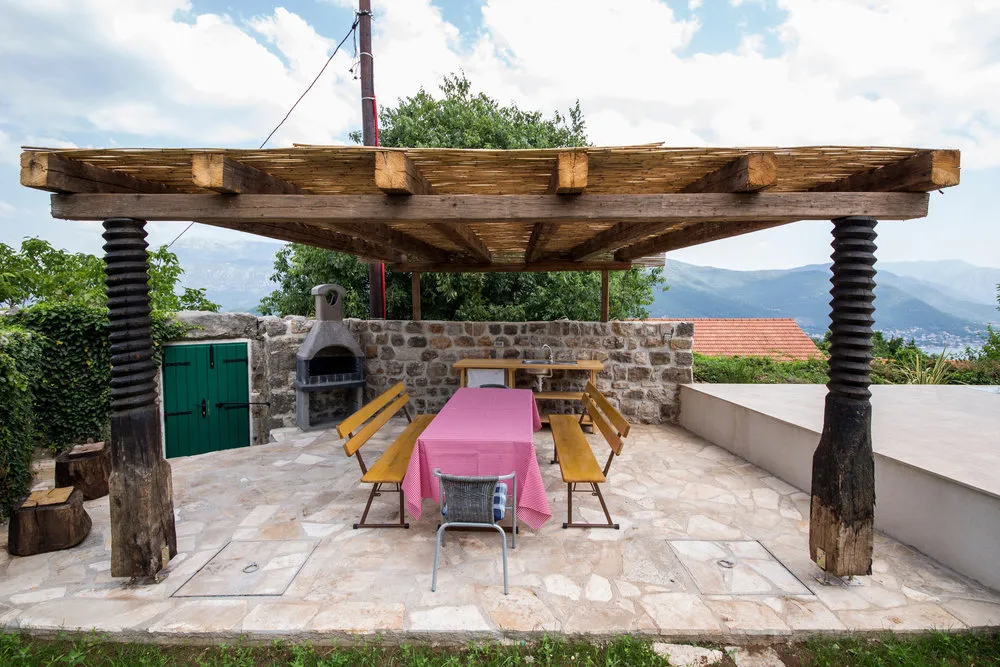 Überdachte Terrasse mit Grill und Essbereich in einer Villa in Luštica, Montenegro: Steinverkleidung und Bergblick.