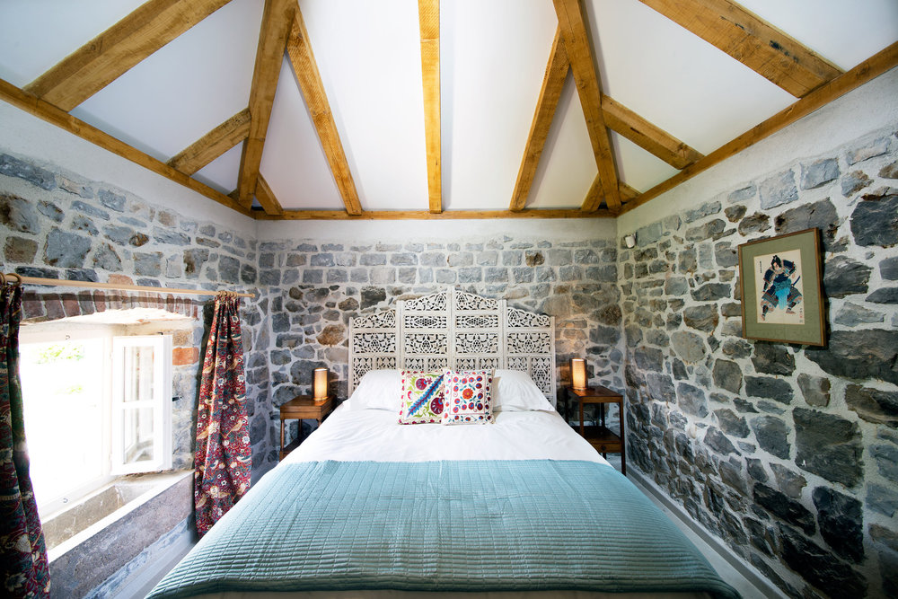 Schlafzimmer in einer Steinvilla auf der Halbinsel Luštica, Montenegro: Bett mit geschnitztem Kopfteil und Holzbalken an der Decke.