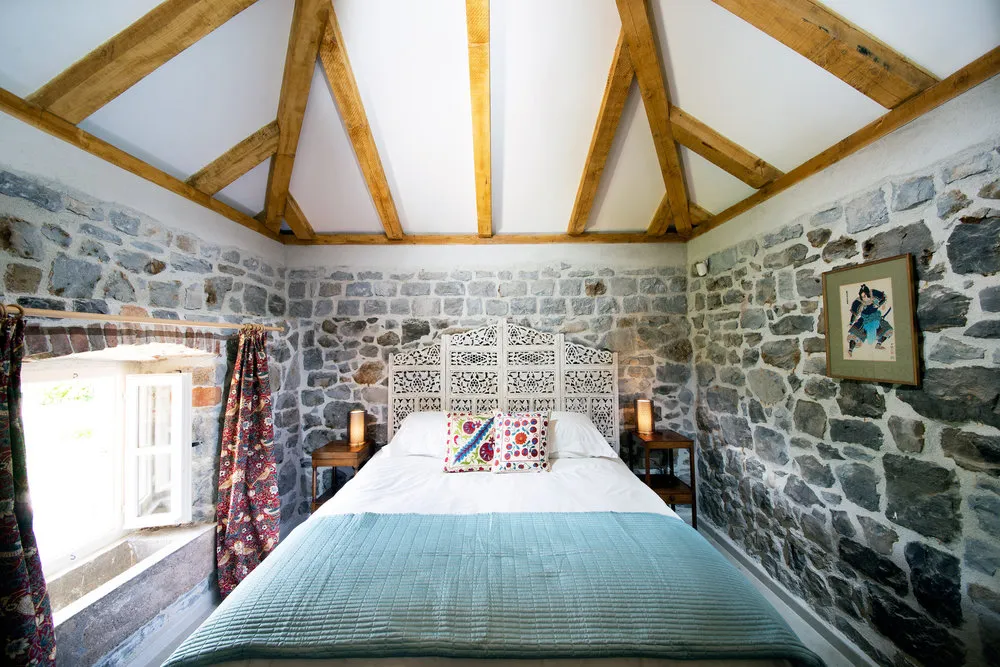 Schlafzimmer in einer Steinvilla auf der Halbinsel Luštica, Montenegro: Bett mit geschnitztem Kopfteil und Holzbalken an der Decke.