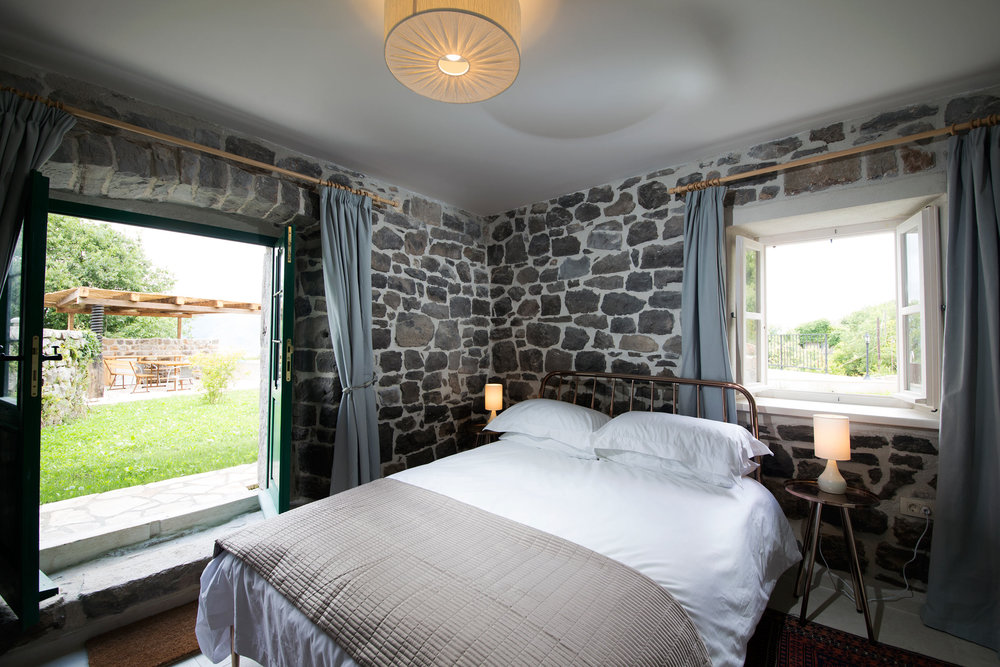 Schlafzimmer in einer Steinvilla auf der Halbinsel Luštica, Montenegro: Doppelbett, Zugang zur Terrasse und zum Garten.