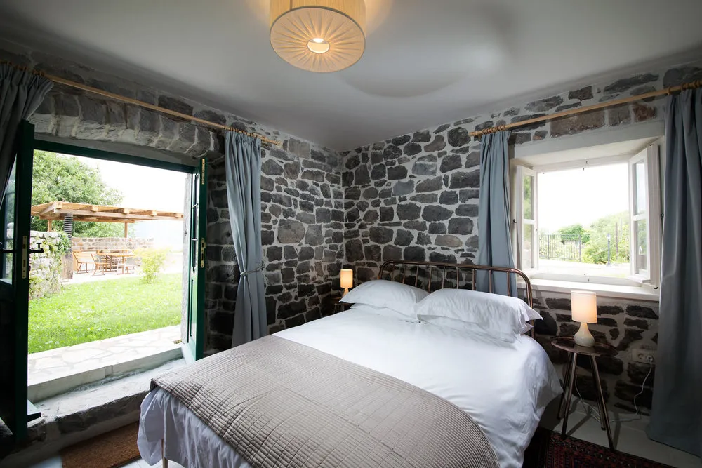 Schlafzimmer in einer Steinvilla auf der Halbinsel Luštica, Montenegro: Doppelbett, Zugang zur Terrasse und zum Garten.