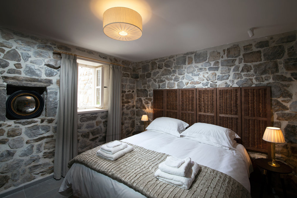 Schlafzimmer mit Steinwänden und einem geflochtenen Kopfteil des Bettes in einer Villa in Luštica, Montenegro.
