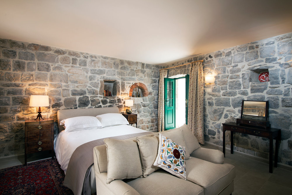 Schlafzimmer in einer Villa in Luštica, Montenegro: Steinwände, ein Doppelbett, ein Sofa und antike Möbel im Interieur.