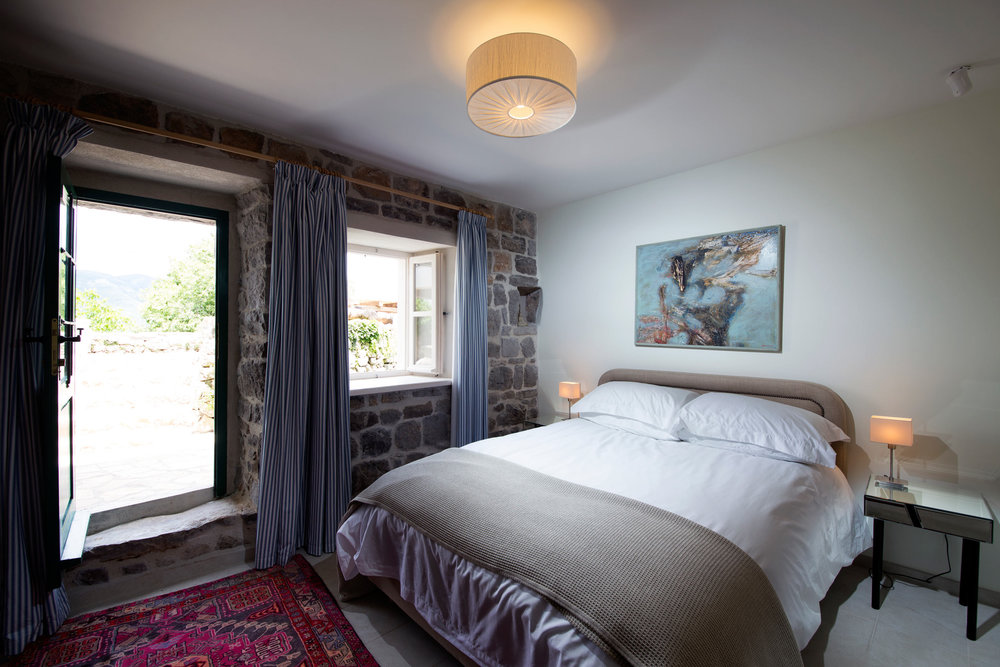 Schlafzimmer in einer Villa in Luštica, Montenegro: Steinwände, Doppelbett, Zugang zur Terrasse und Vintage-Teppich.