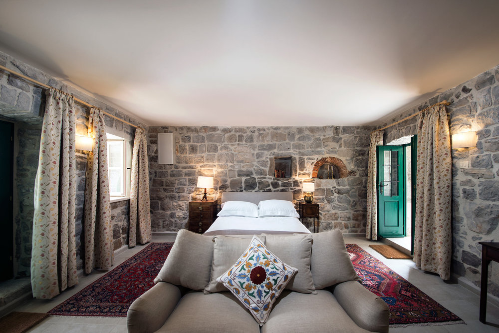 Schlafzimmer in einer Steinvilla auf der Halbinsel Luštica, Montenegro: Bett, Vintage-Möbel und authentisches Mauerwerk aus Stein.