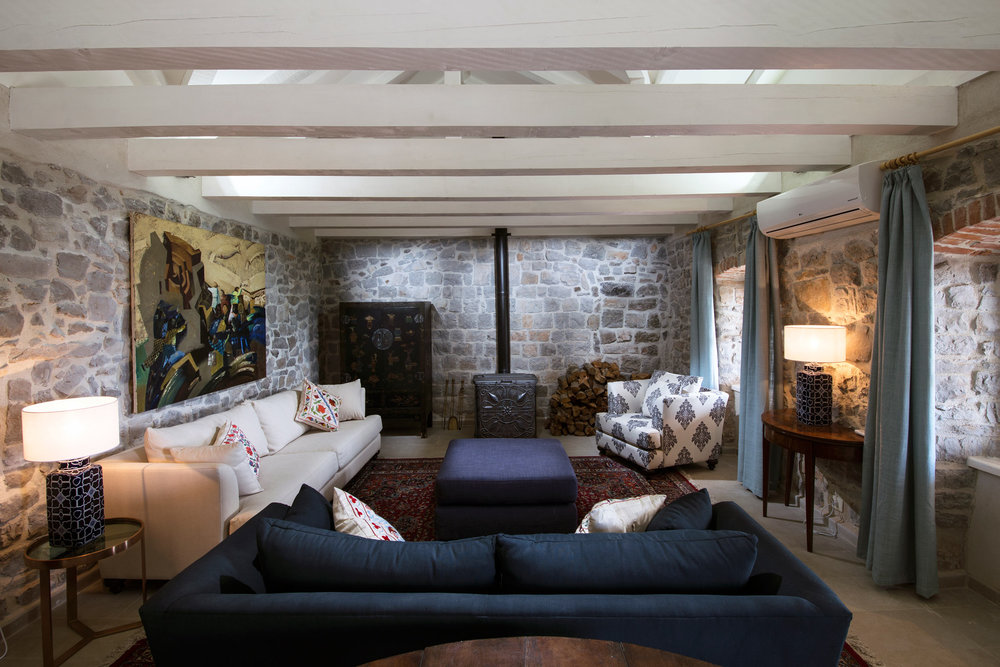Wohnzimmer in einer Villa in Luštica, Montenegro: Steinwände, Holzbalken, Kamin und stilvolle Polstermöbel.
