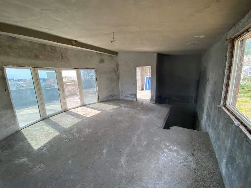 Dnevna soba bez završne obrade u kući u izgradnji u Šušnju, Crna Gora: betonski zidovi, panoramski prozori i izlaz na terasu.