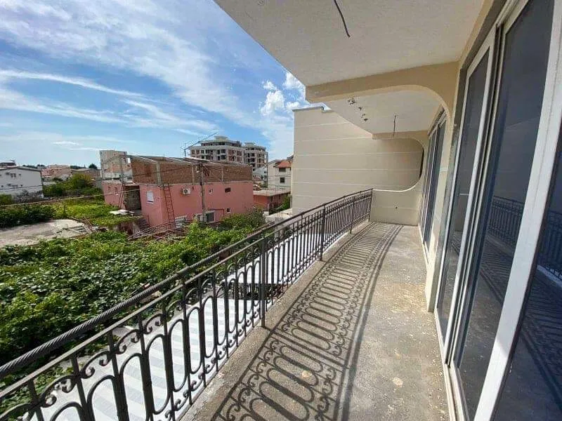Prostran balkon sa kovanom ogradom u kući u Šušnju, Crna Gora, pogled na grad i zelenu površinu.
