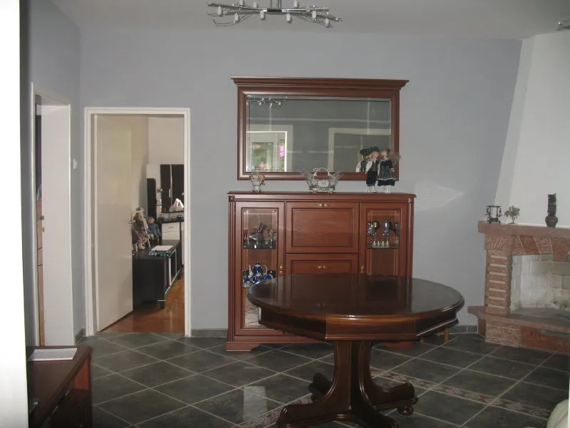 Ein geräumiges Wohnzimmer mit dunklen Holzmöbeln, einem runden Esstisch und einem dekorativen Kamin.