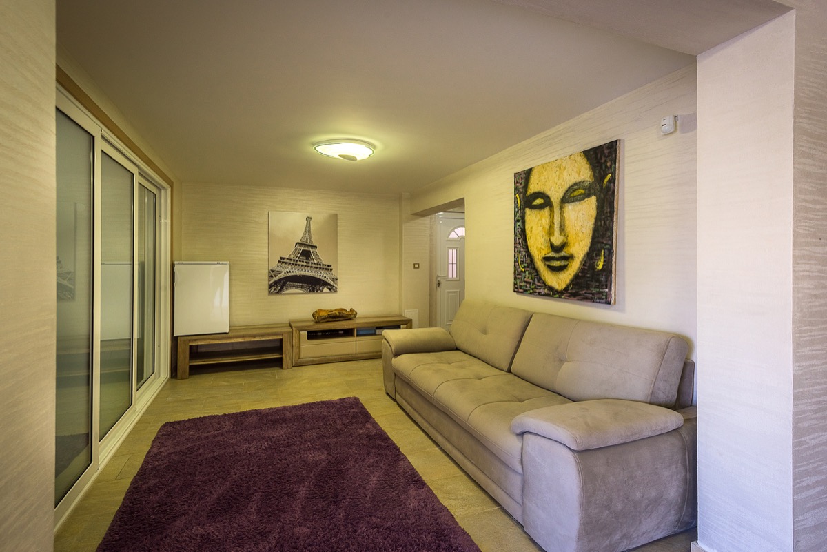 Wohnzimmer in einer Villa in Krašići, Montenegro: beiges Sofa, violetter Teppich, Gemälde an den Wänden und Panoramaverglasung.