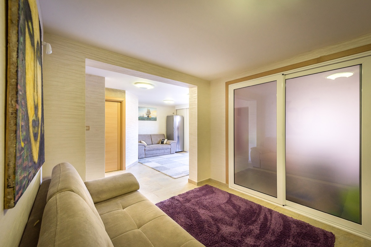 Wohnzimmerinterieur einer Villa in Krašići, Montenegro: helle Möbel, Panoramafenster und ein gemütlicher violetter Teppich.