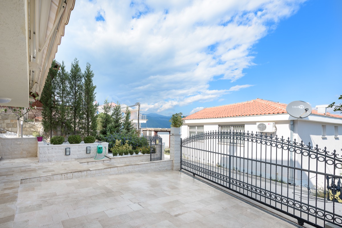 Terrasse und Einfahrt zur Villa in Krašići, Montenegro: Steinverkleidung, schmiedeeiserne Tore, Landschaftsgestaltung und Bergblick.