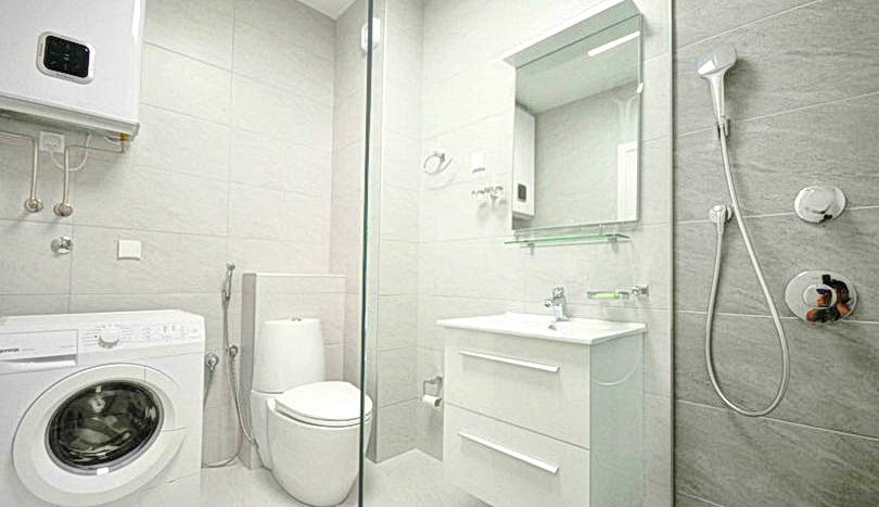 Budva, Karadağ’daki konut kompleksinde duş kabini ve çamaşır makinesi bulunan modern banyo. Açık renkli fayanslar ve sıhhi tesisat.