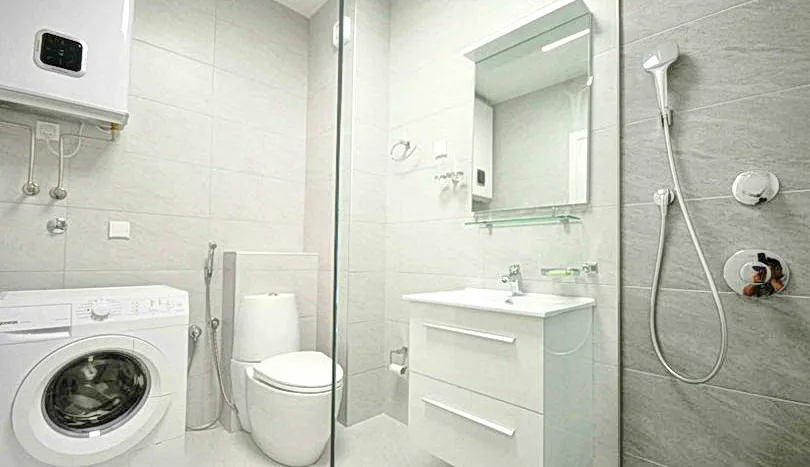 Modernes weißes Badezimmer mit Waschmaschine, Toilette, Waschbecken, Spiegel und Dusche.