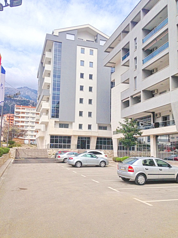 Karadağ, Budva'da otoparklı modern konut kompleksi: binaların cephesi, panoramik pencereler ve dağ manzarası.