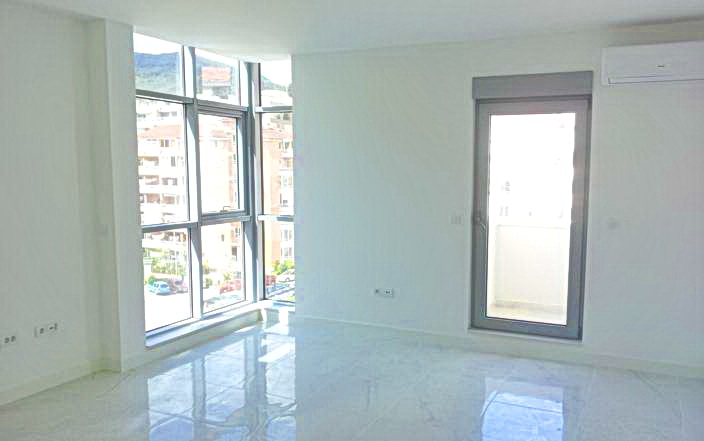 Panoramik pencereli ve balkona çıkışı olan aydınlık oturma odası, yeni konut kompleksinde, Budva, Karadağ.