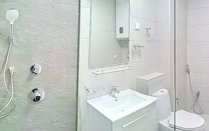 Budva, Karadağ’daki bir konut kompleksinde duş kabinli modern banyo: açık renkli fayanslar ve sıhhi tesisat.