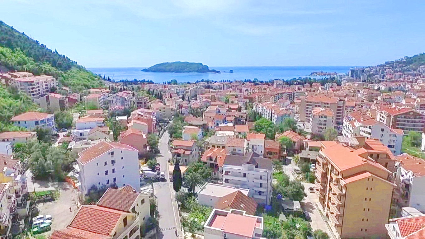 Panoramablick auf die Stadt Budva in Montenegro, Wohnhäuser mit roten Dächern, Berge und die Insel Sankt Nikolaus am Horizont