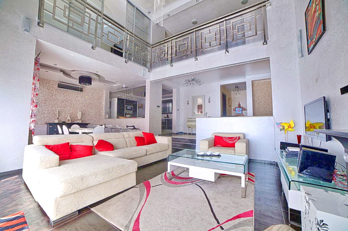 Geräumiges Wohnzimmer mit doppelter Raumhöhe in einer Villa in Budva, Montenegro: helles Sofa, Glastisch und moderne Dekoration.
