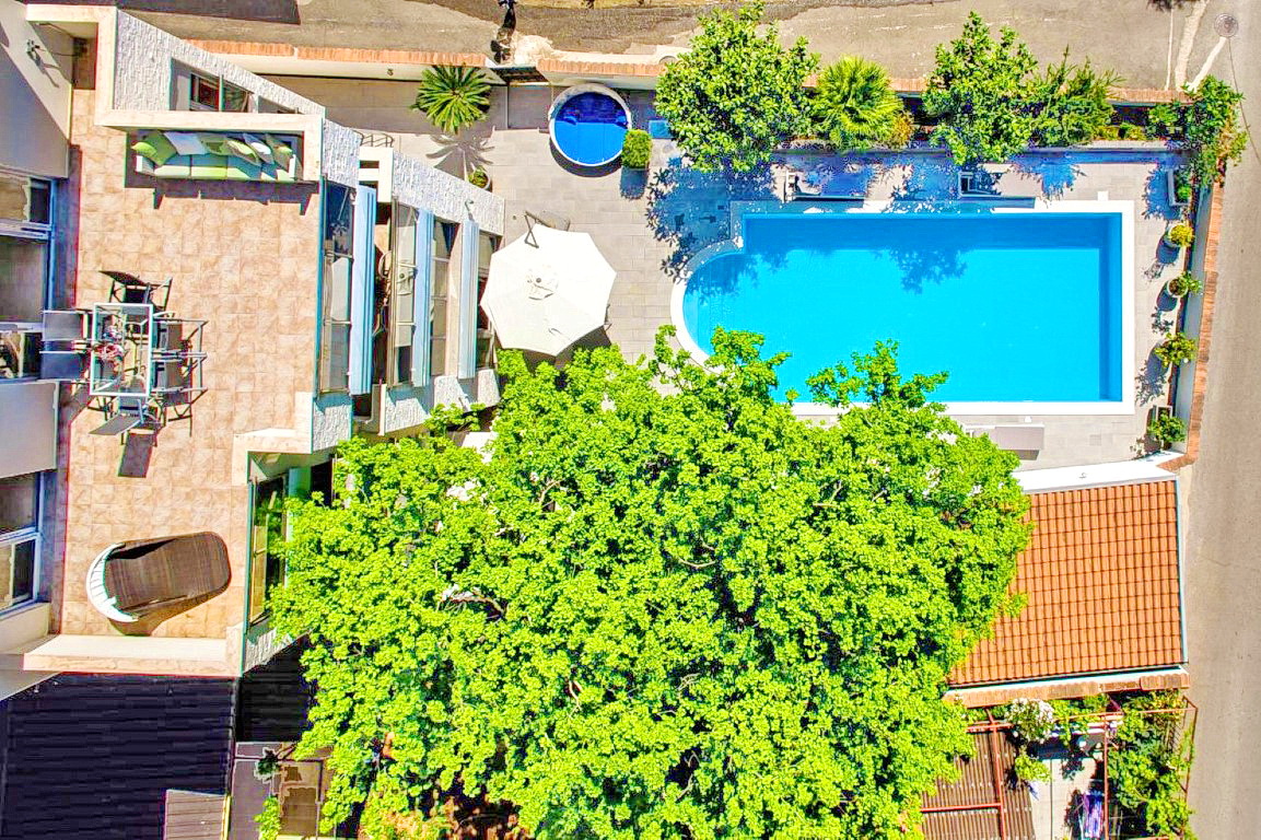 Blick von oben auf eine Villa in Budva, Montenegro: offene Terrasse mit Möbeln, Pool, Whirlpool und Garten mit großem Baum.