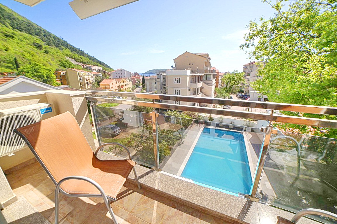 Blick vom Balkon der Villa in Budva, Montenegro: Terrasse mit Sessel, Panoramablick auf den Pool, die Berge und die städtische Bebauung.