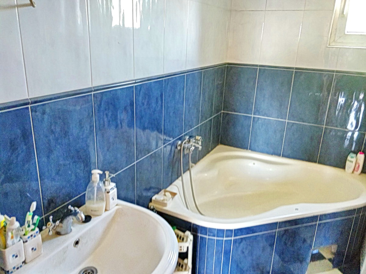 Kupatilo sa ugaonom kadom i plavim pločicama u kući na prodaju, Podgorica, Crna Gora.