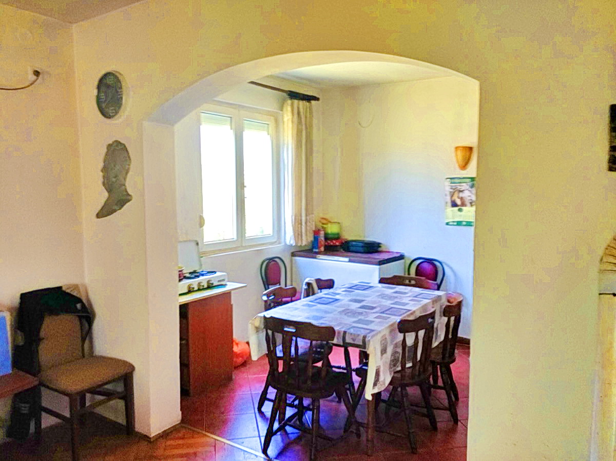 Kuhinja-trpezarija u kući u Podgorici, Crna Gora: trpezarijski sto, drvene stolice, lučni otvor i pločice na podu.